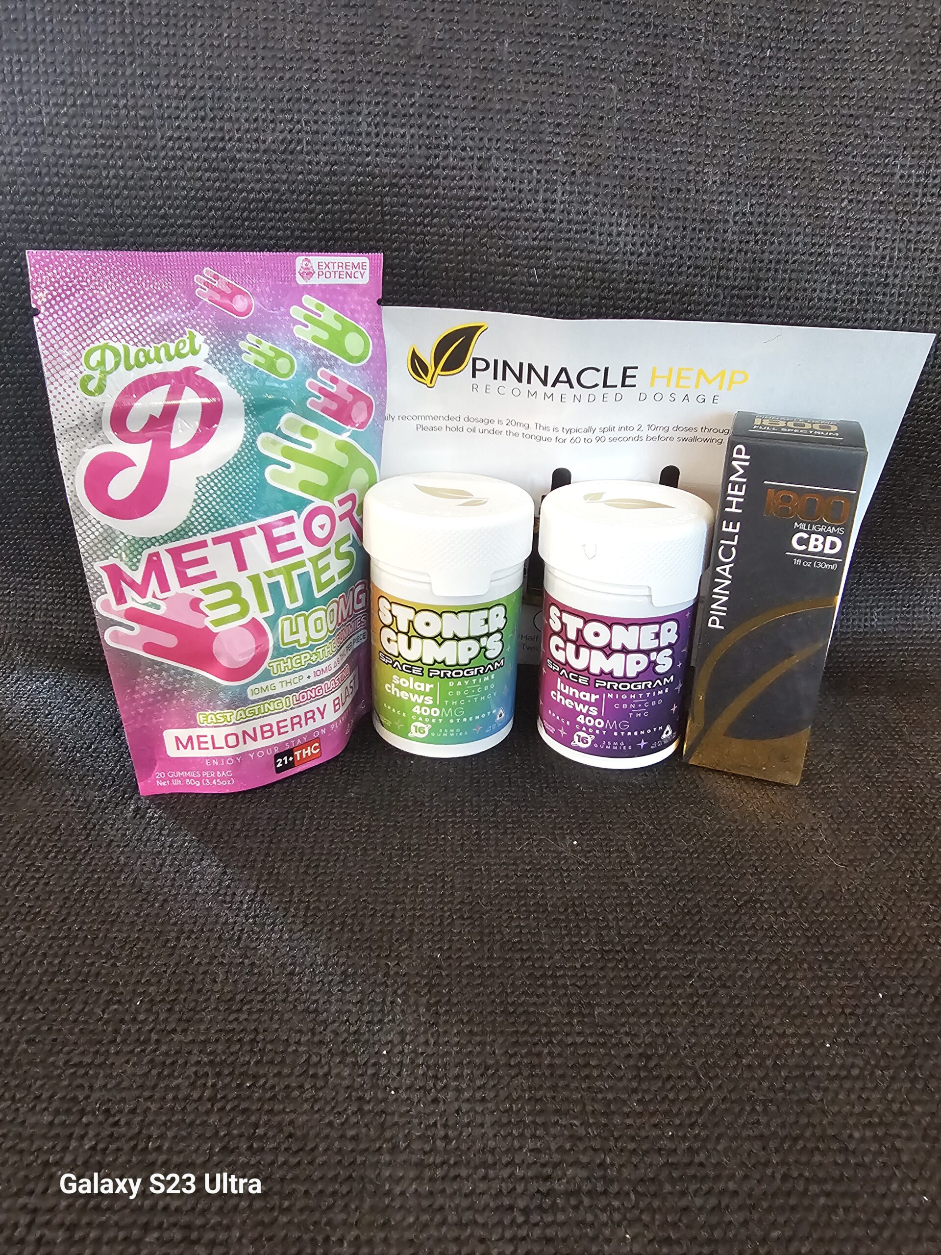 Stoner Gump Solar and Lunar Chews, Pinnacle Hemp CBD tincture and Planet P Meteorbites arranged on a black background